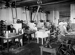 Pakking av brisling. i Egelands Hermetikkfabrikk, Kopervik, ca. 1910-1920. Kvinnene gjer eskene klare medan mennene opererer falsemaskina.  Foto: Hakon Johannessen. Stavanger Byarkiv.